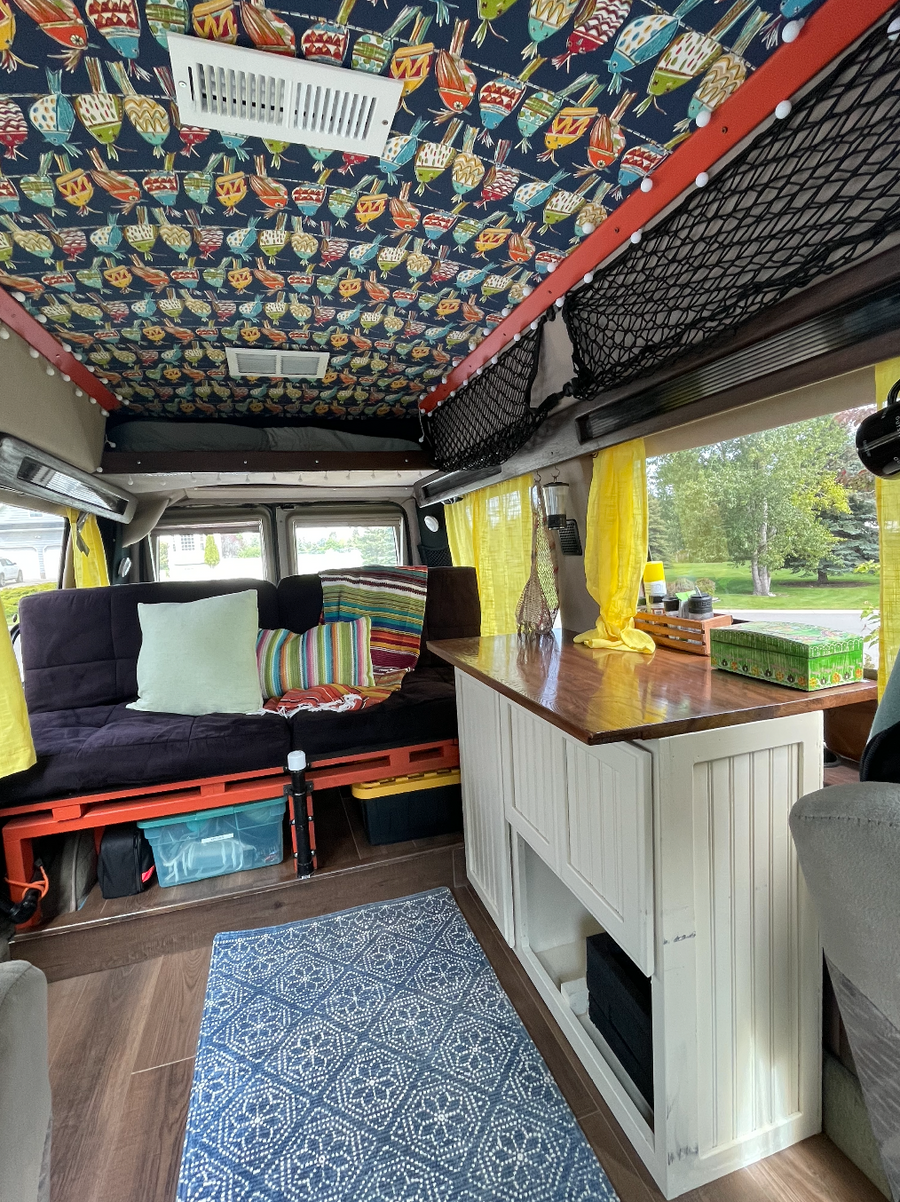 RV rental: Inside a cozy camper van featuring a vibrant bird-patterned ceiling, comfy futon, wood counter, and storage.