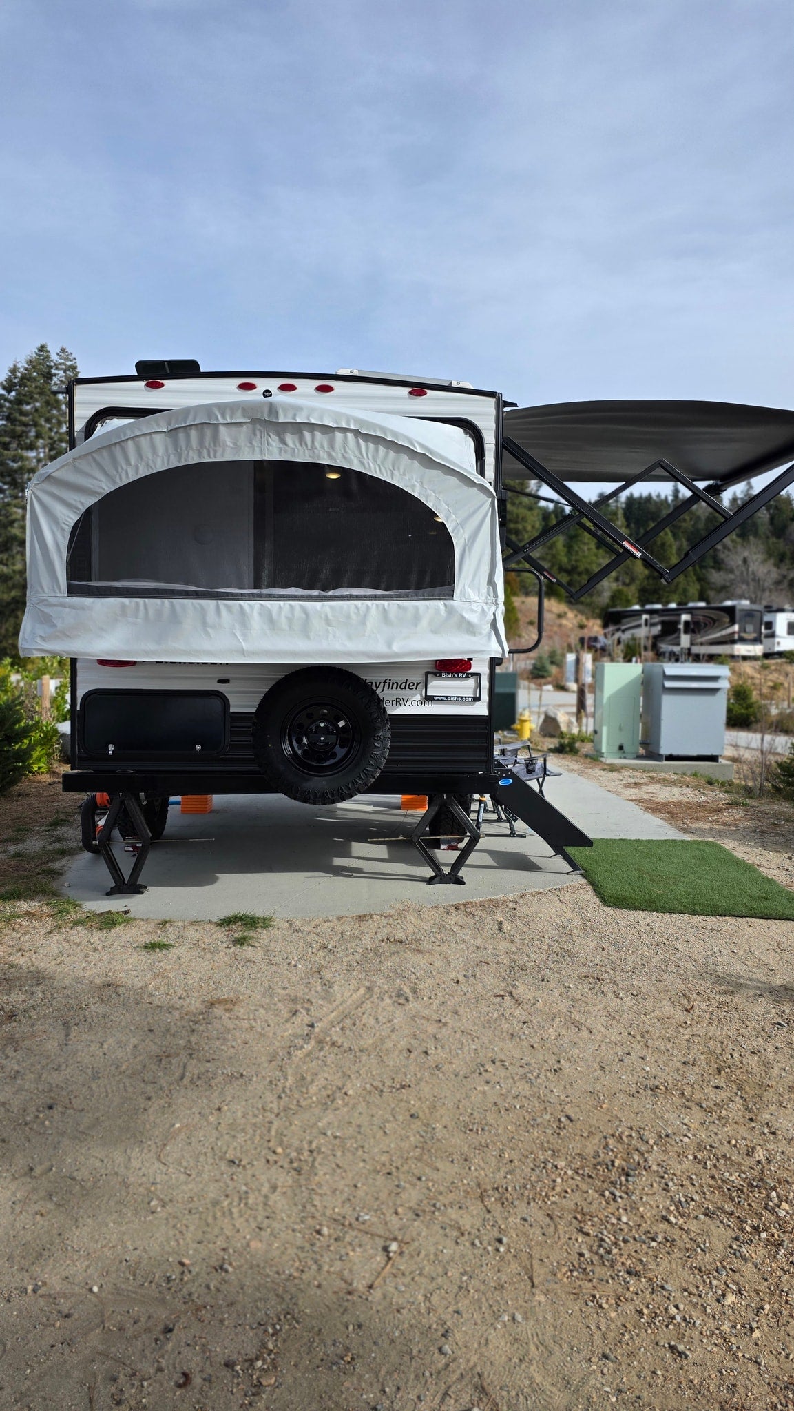 Back of an RV rental pop-up travel trailer with extended bed, awning, and leveling jacks at a campsite. Perfect for camping. — photo 17