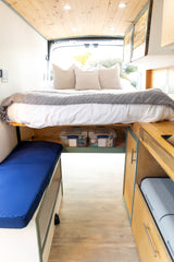 Explore this rv rental's functional camper van interior: elevated bed, organized kitchen storage, and cozy bench seating.
