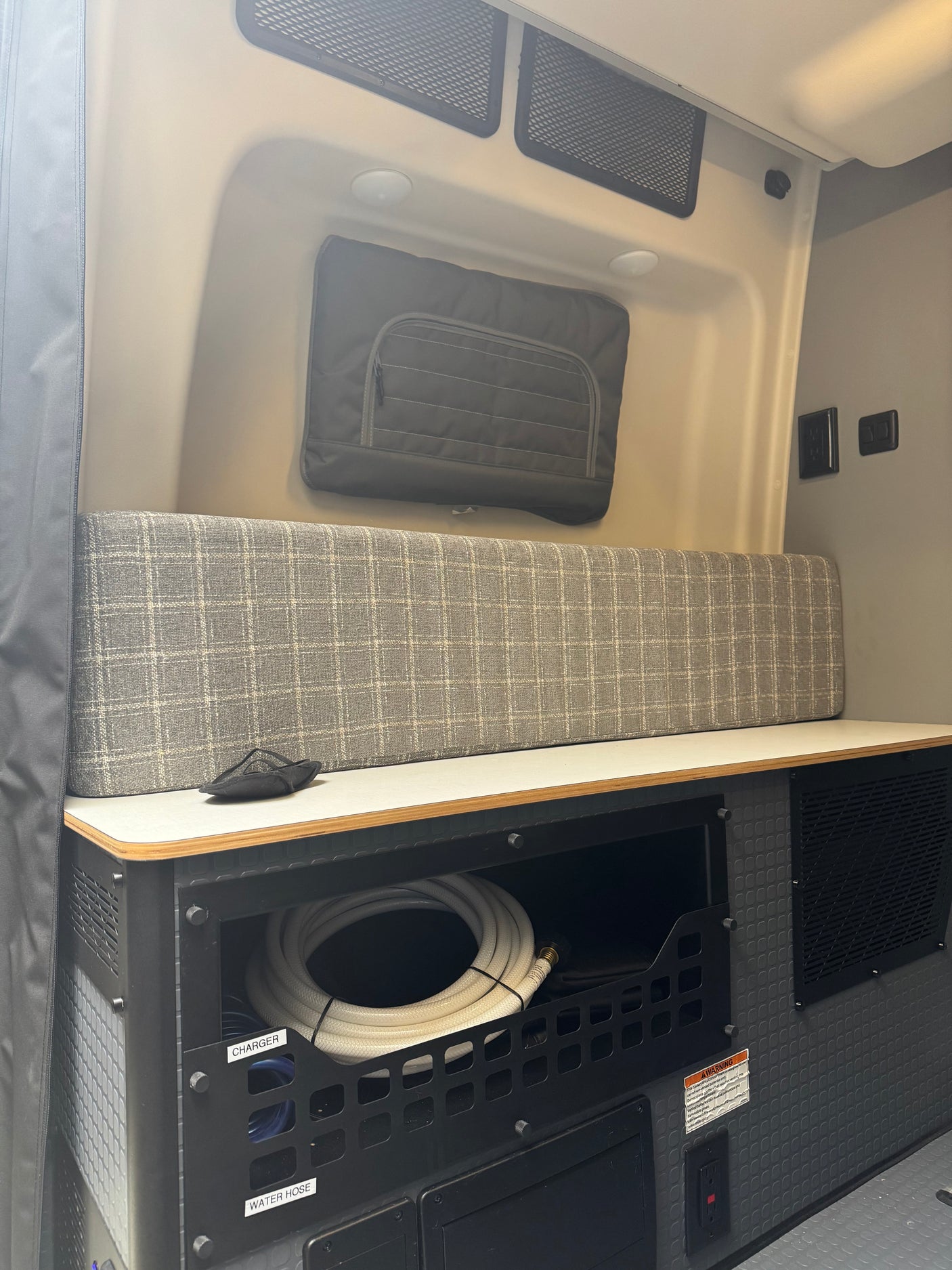 RV rental interior featuring organized utility storage with a water hose, comfy bench, and power outlets for mobile living.