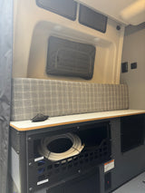 RV rental interior featuring organized utility storage with a water hose, comfy bench, and power outlets for mobile living.