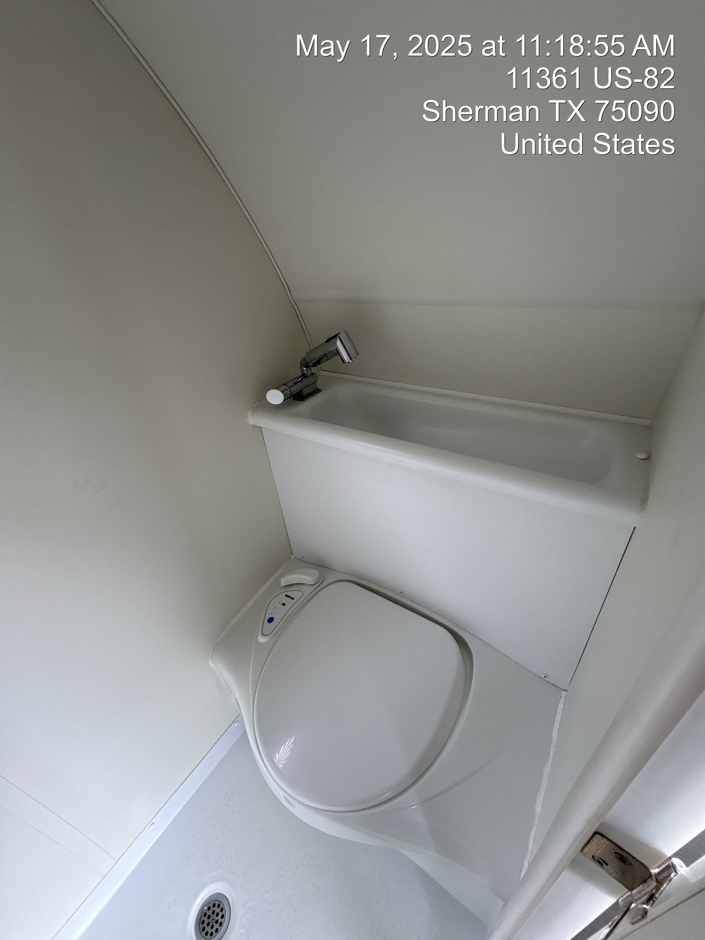 This clean, compact RV rental bathroom features a toilet, a small sink with a faucet, and a shower area with a drain.