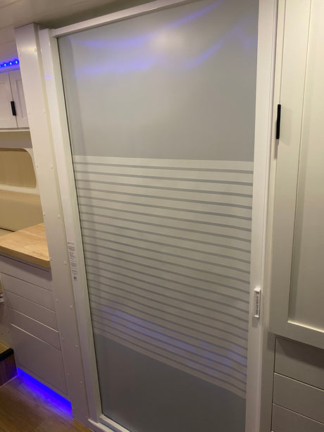 Modern RV rental interior featuring a space-saving Nautilus retractable shower door, sleek white cabinetry, and blue accent lighting.