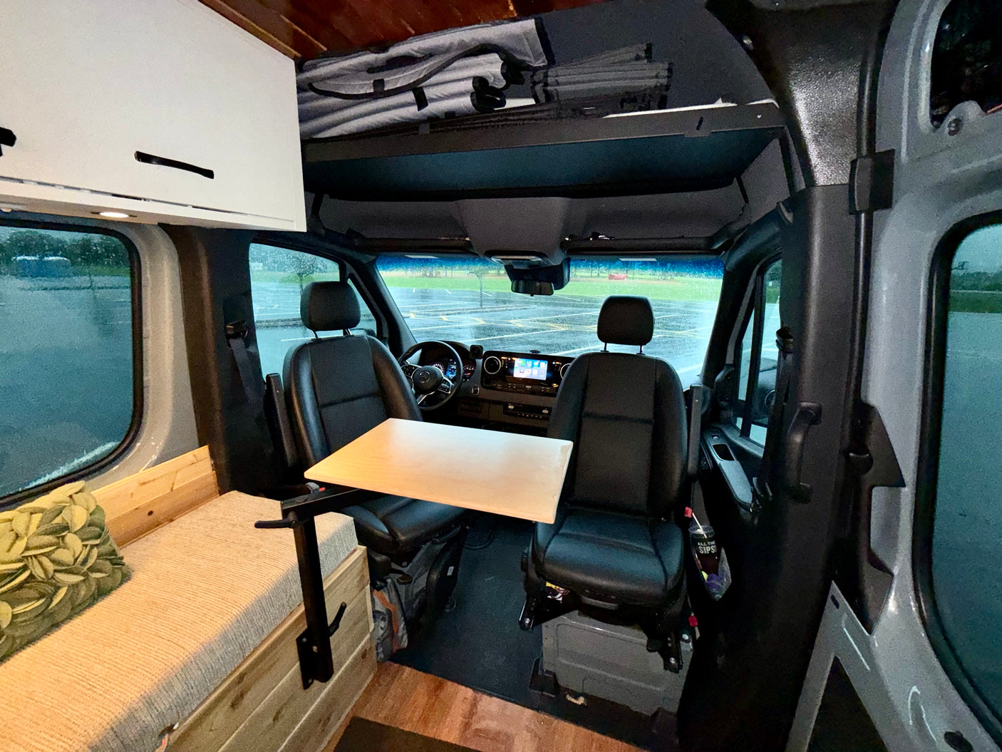 Inside this RV rental, see the campervan's compact living area with swivel front seats, a fold-out table, and cozy bench seating.