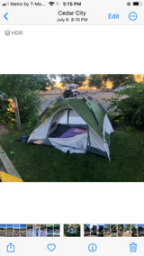 Green tent on grass, with sleeping gear inside, at a Cedar City campground. RV rental parked nearby for camping.