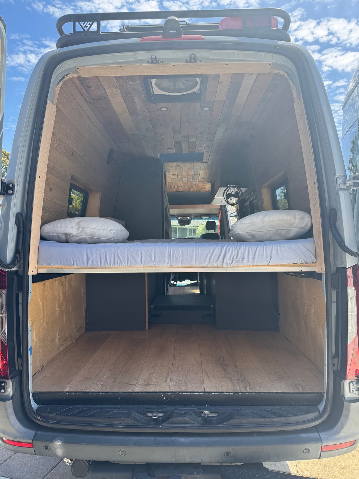 This rv rental reveals a spacious camper van interior with a raised bed, wood-paneled walls/ceiling, and ample storage. — photo 8