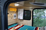 Inside a cozy RV rental: a comfortable bed with colorful blanket, window views, and warm lighting, perfect for travel.