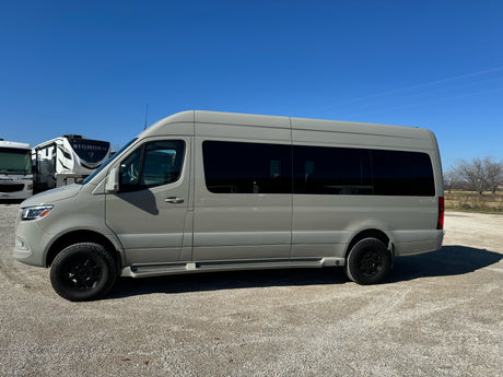 Light grey Sprinter van with tinted windows and black wheels, ready for rv rental adventures. Parked on gravel, clear sky.