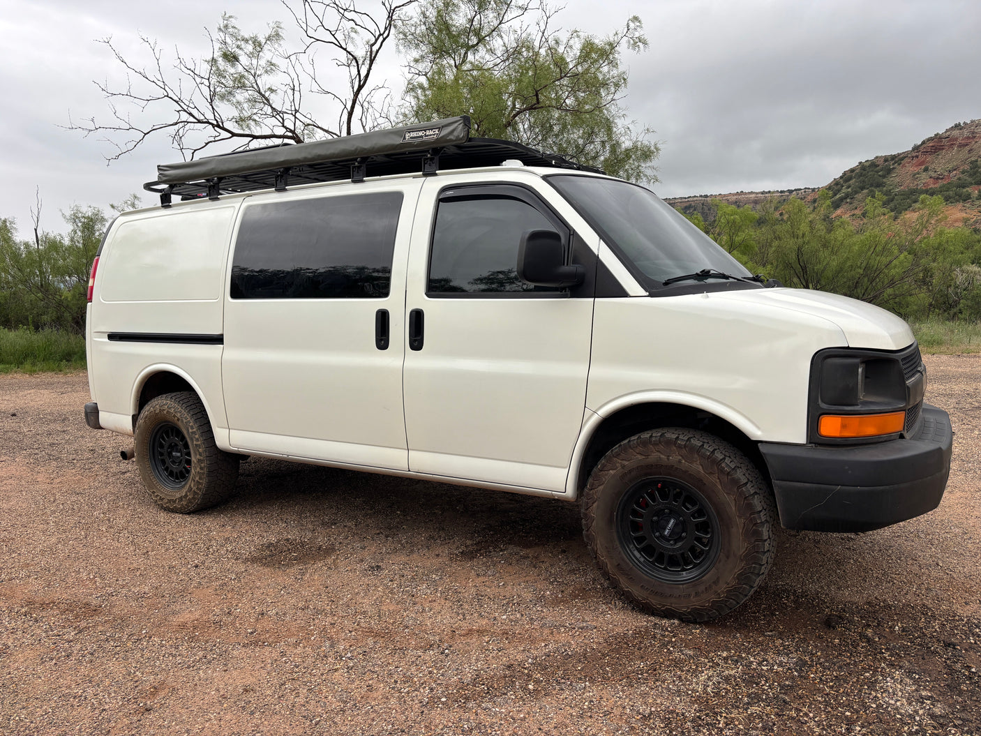 White Chevy off-road van with Rhino-Rack awning, all-terrain tires. Perfect RV rental for adventure.