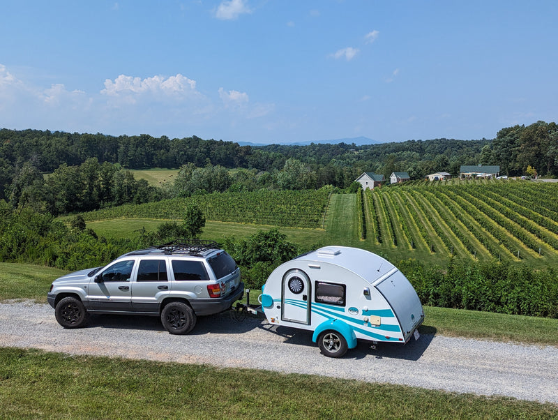 Scenic vineyard view! Silver SUV towing a white teardrop camper, perfect for an rv rental road trip. Green hills & blue sky. — photo 18