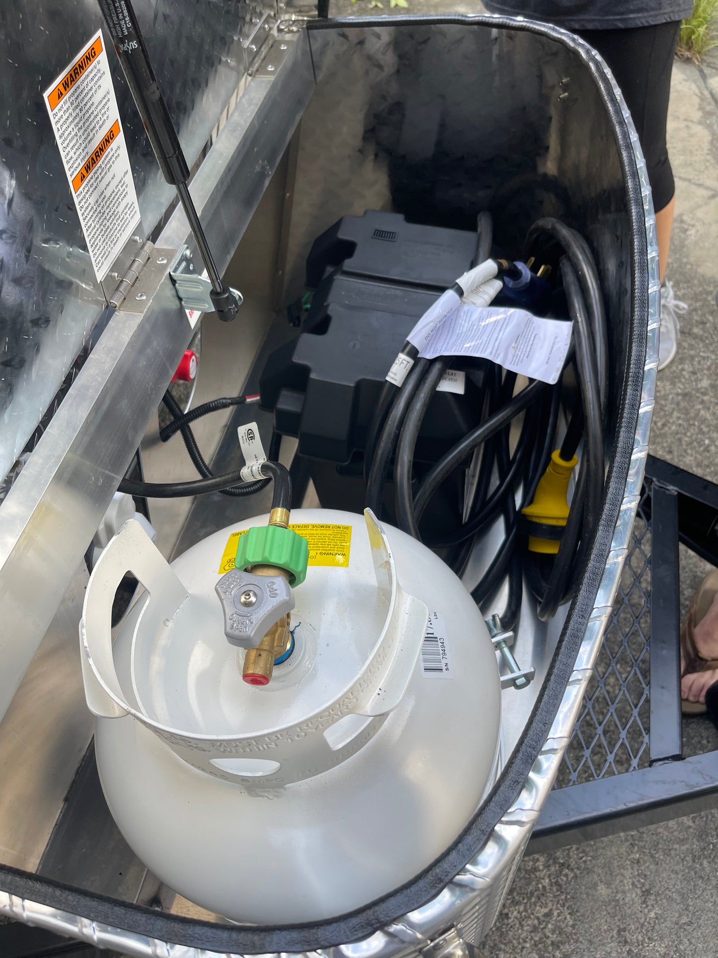 RV rental storage compartment with propane tank, batteries, & electrical cables. Essential utilities for the road.