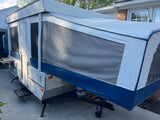 This white and blue pop-up camper, ideal for an RV rental, is fully set up with mesh windows, ready for outdoor adventures.