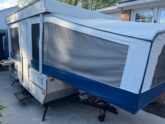 This white and blue pop-up camper, ideal for an RV rental, is fully set up with mesh windows, ready for outdoor adventures.
