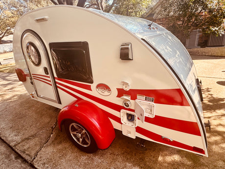 Red and white teardrop camper, ideal for RV rental adventures, parked on a sunny driveway.