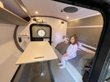 Happy girl in pajamas inside a cozy RV rental, featuring a bed, table, and smart storage for comfortable travel.