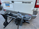 Rear of a white Dodge Sprinter RV rental with Nevada plates and a black Vibrelli bike rack attached.