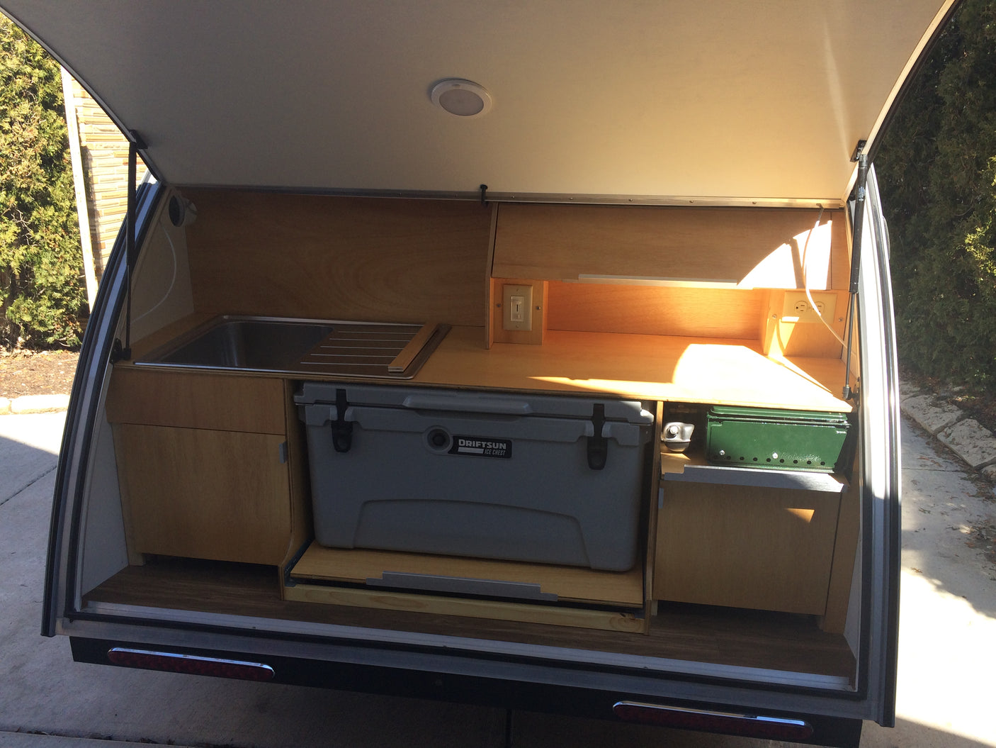 RV rental teardrop trailer's open rear galley with a sink, cooler, stove, and wooden cabinetry for camping.