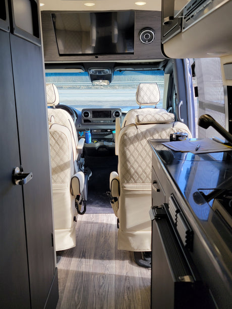 Explore this luxury RV rental interior: plush, diamond-stitched cream seats, modern dashboard, and TV area.
