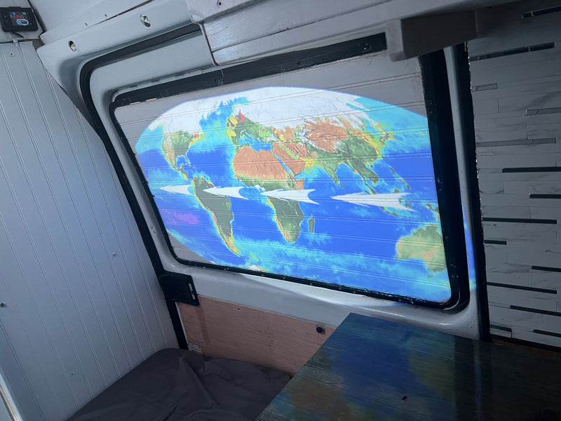 Inside an RV rental, a vibrant world map is projected onto horizontal window blinds, suggesting travel dreams. — photo 2