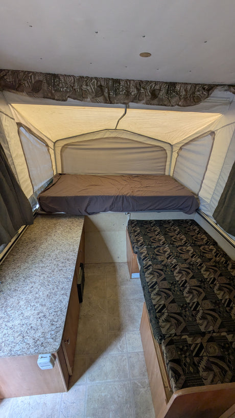 Inside an rv rental pop-up camper featuring a bed, patterned bench/bed, and countertop. Ideal for camping trips.