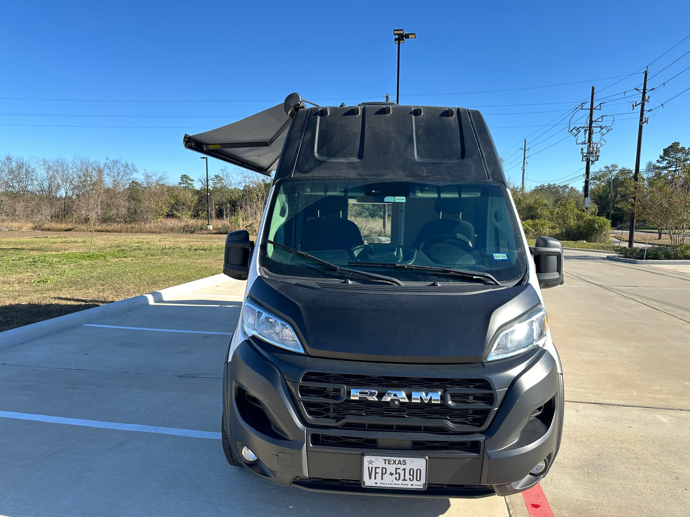Front view of a white and black Ram ProMaster camper van (RV rental) with an extended awning, parked on a sunny day. — photo 5