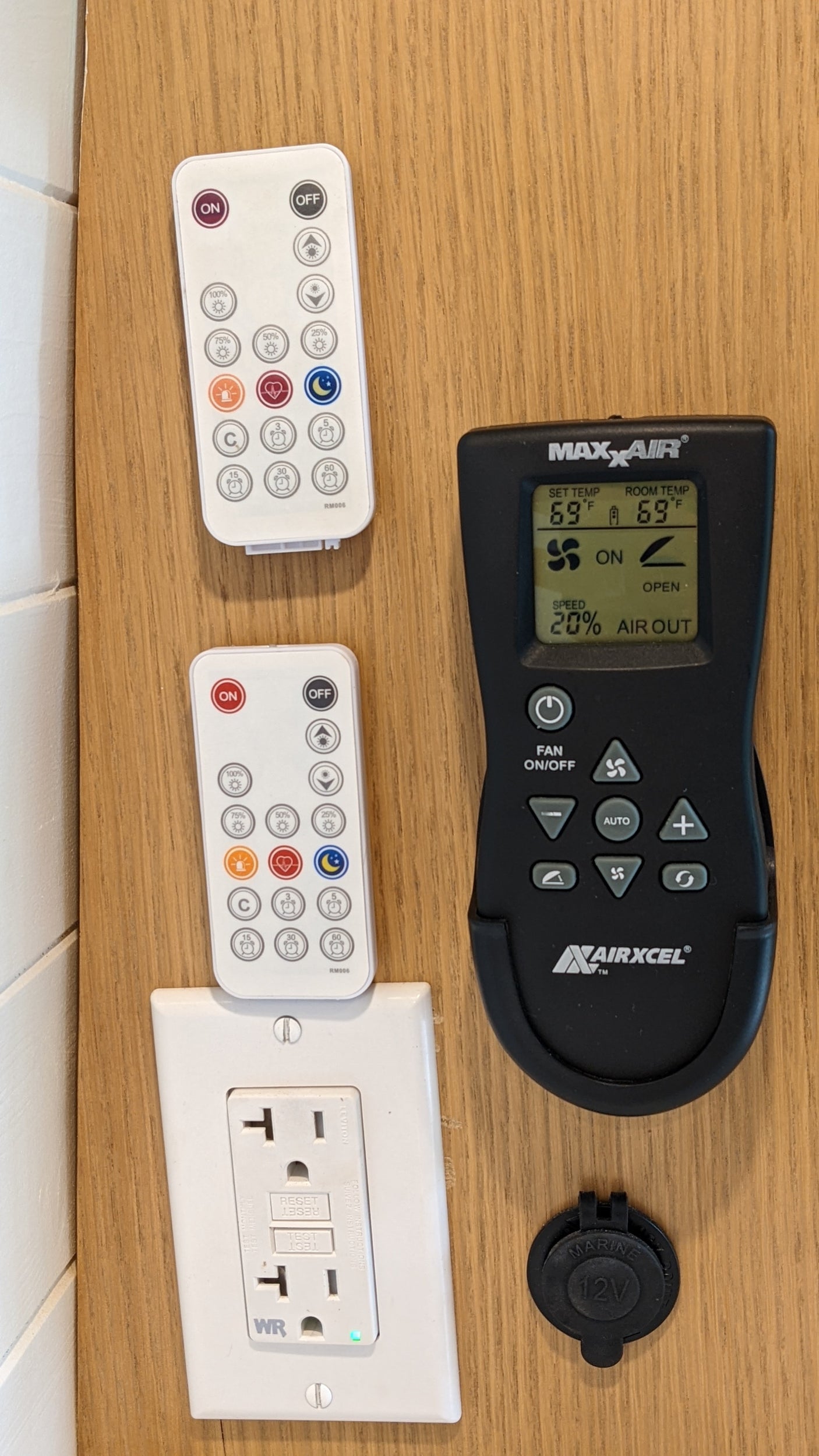 RV rental interior wall with controls: light remotes, MaxxAir fan display, AC outlet, and 12V socket.