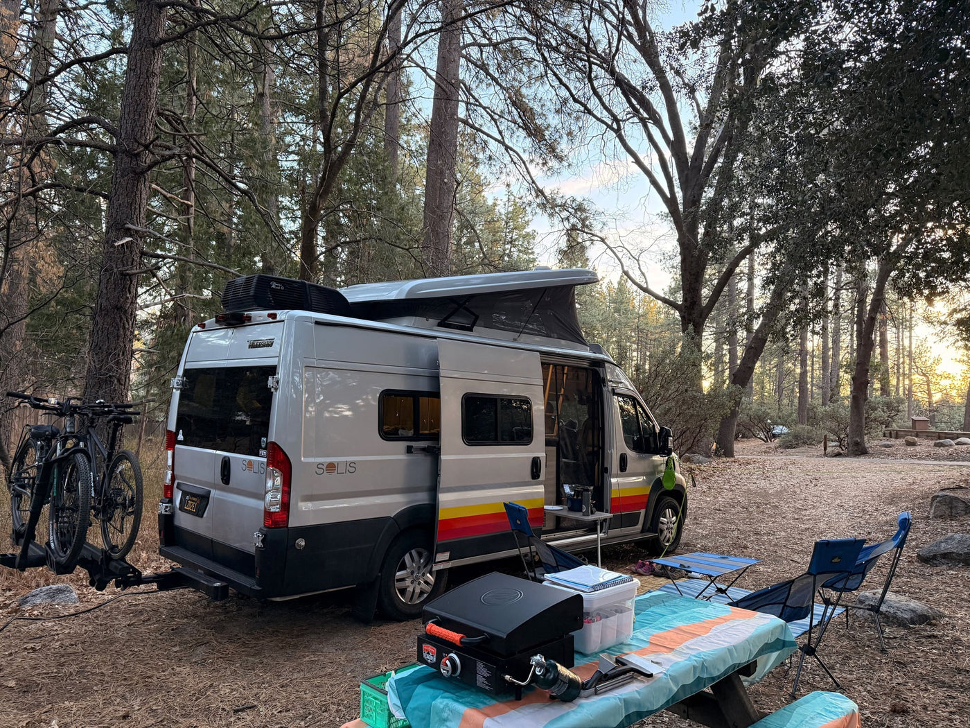  and a dog at a sunny outdoor campsite.|Gray Winnebago Solis RV rental with a pop-top and bike rack — photo 6