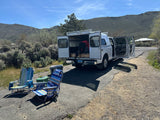 Preparing for adventure with an rv rental. A person packs a truck camper in scenic Nevada, with camp chairs & coolers nearby.