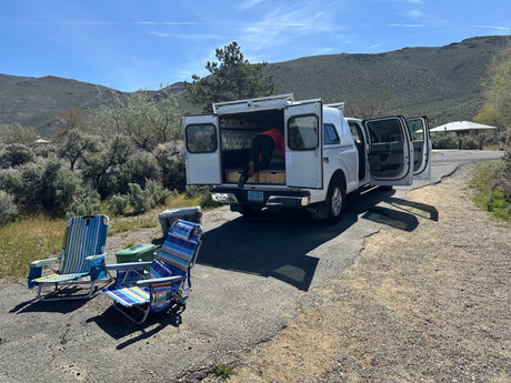 Preparing for adventure with an rv rental. A person packs a truck camper in scenic Nevada, with camp chairs & coolers nearby.