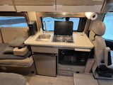 Compact RV rental interior featuring a kitchen with sink, stove, microwave, fridge, and a cozy living space with a sofa.