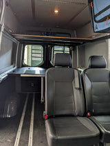 RV rental interior: black passenger seats, floor tracks, and a compact utility counter for versatile travel.