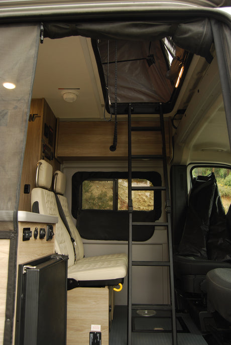 RV rental interior showing a ladder to a pop-top bed, plush seating, and controls for a comfortable camper experience.