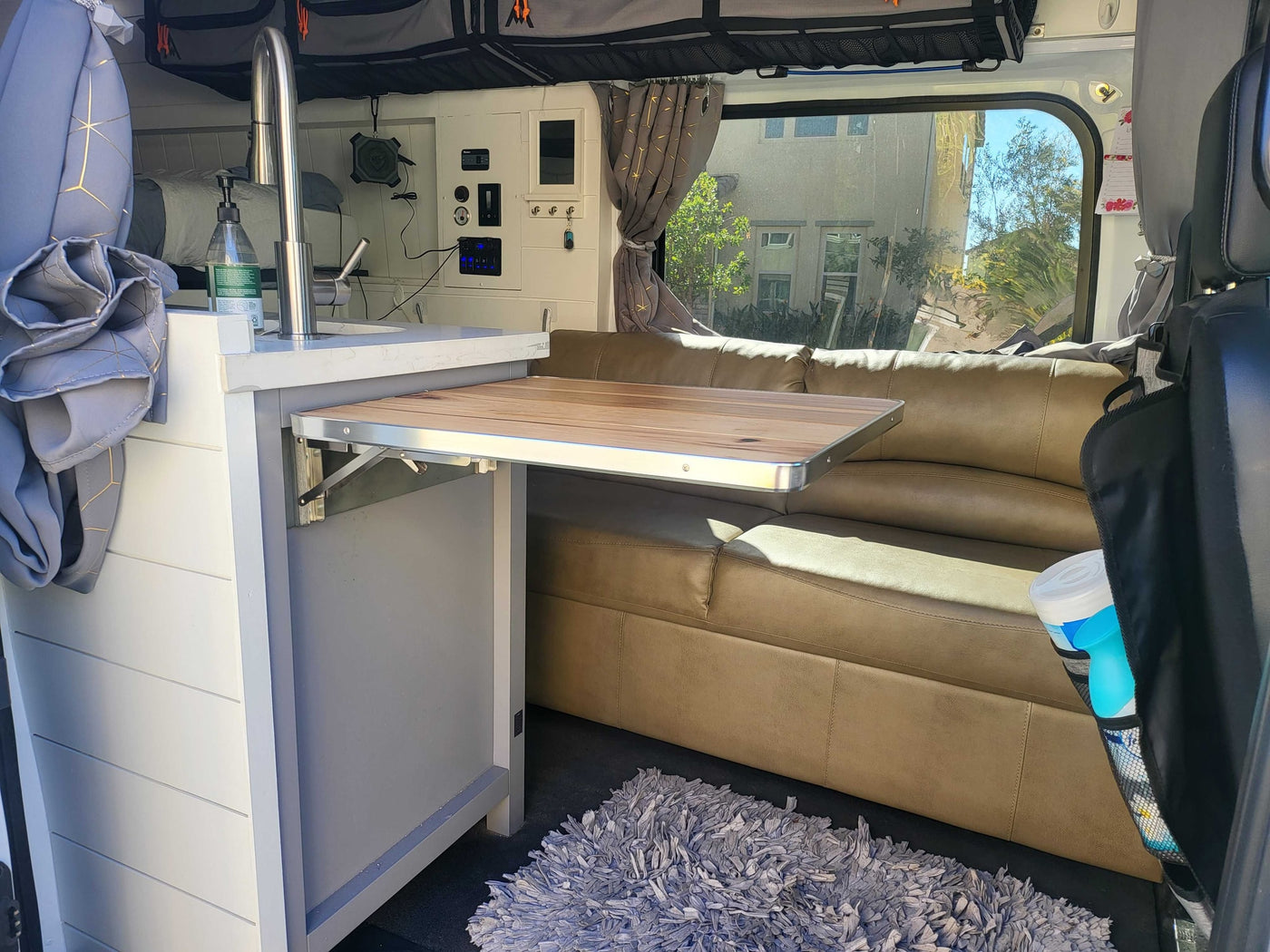 RV rental interior showcasing a compact camper van's functional design: kitchen sink, fold-out table, and cozy sofa. — photo 10
