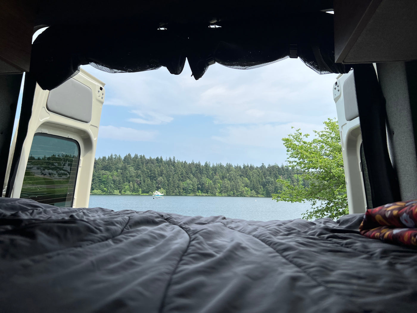 Serene RV rental view from inside: Open van doors showcase a tranquil lake, lush forest, and boat from the comfort of bed. — photo 4