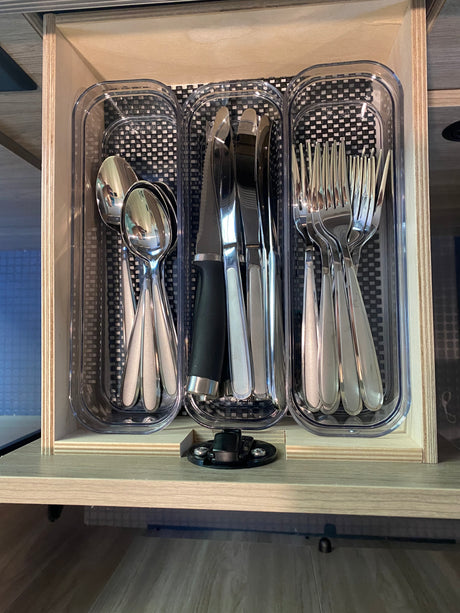RV rental: Organized kitchen drawer with silver spoons, knives, & forks in clear plastic organizers on a checkered mat.