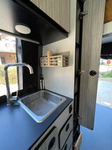 This rv rental features a well-equipped kitchen with a stainless steel sink, chrome faucet, and wall-mounted spice rack.