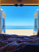 RV rental: View from inside, legs under plaid blanket, open van doors reveal beach & ocean.
