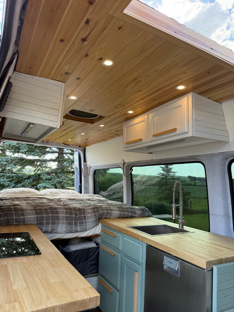 Cozy RV rental interior with a wood-paneled ceiling, bed, and full kitchen, offering scenic views for your trip.