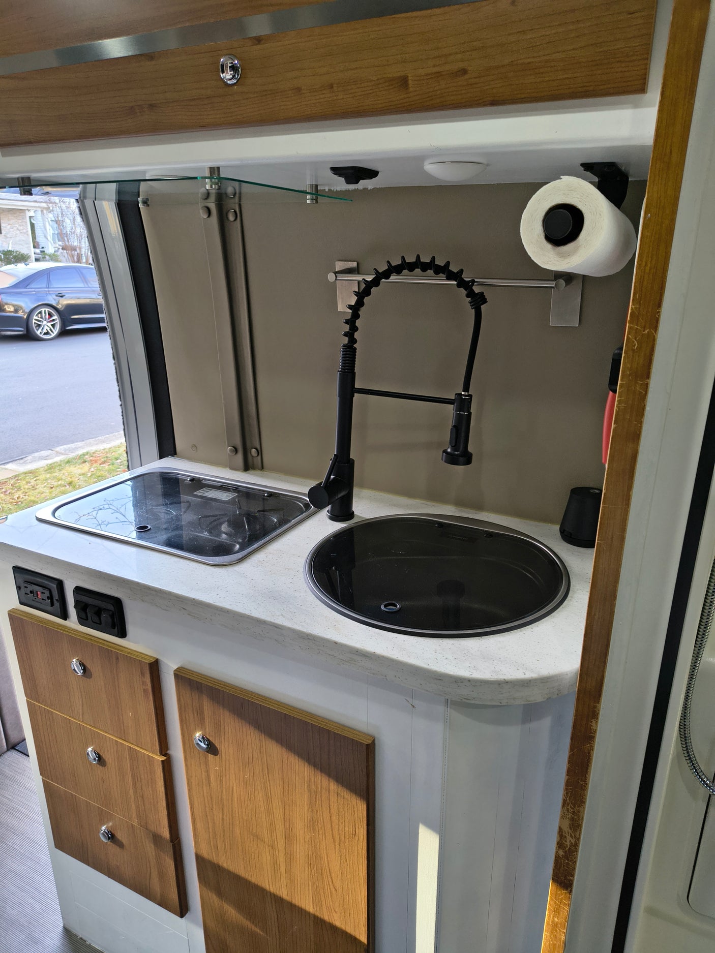RV rental kitchen: Features a black sink, flexible faucet, integrated stovetop, and wooden cabinets for an efficient space.