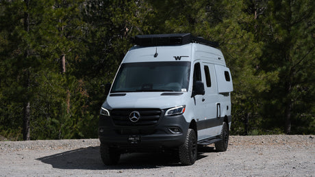 Adventure-ready Mercedes-Benz Sprinter RV rental on a gravel forest road, ideal for outdoor travel.