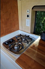 This RV rental's kitchen features a two-burner stove, light wood cabinetry, and various outlets for comfortable mobile living.
