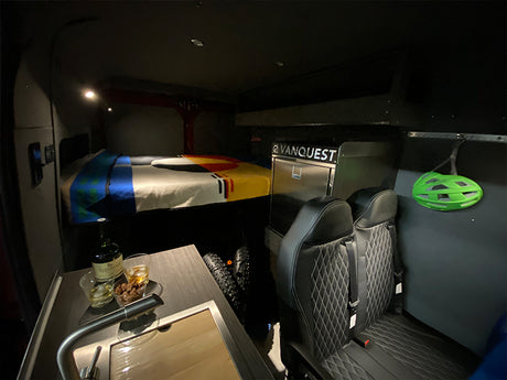 Cozy RV rental interior showing a raised bed, kitchen, passenger seats, and bike storage, perfect for adventure.