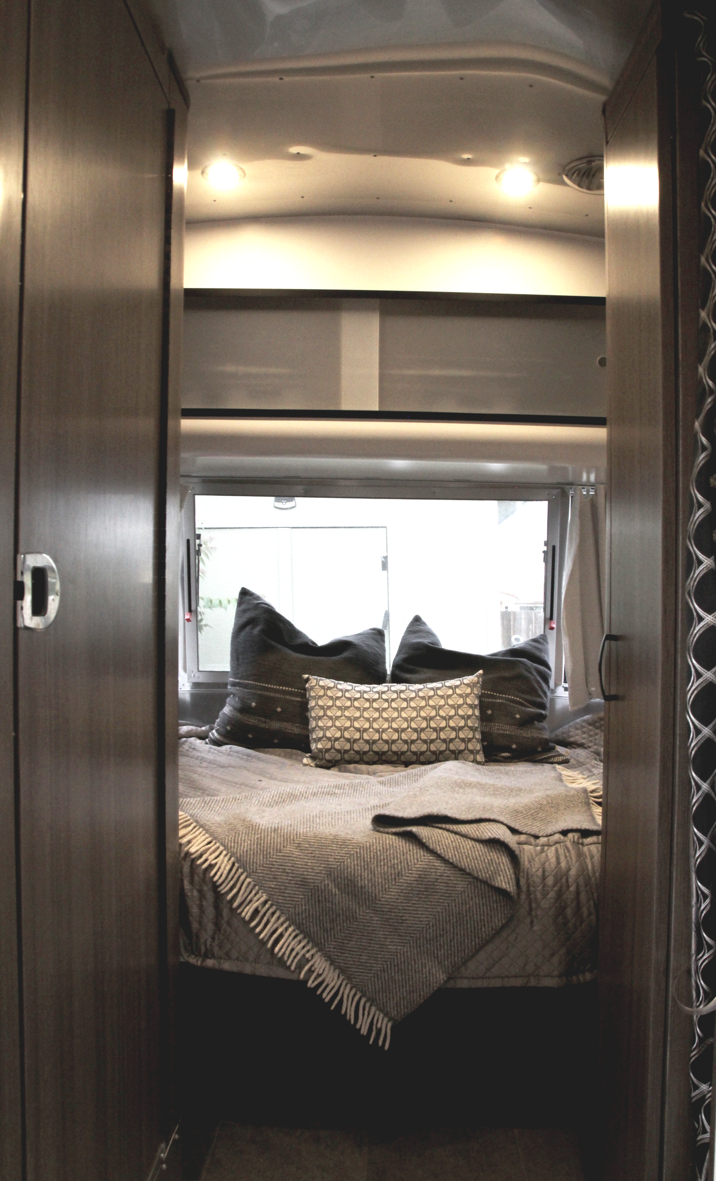 Inside an RV rental: a modern bedroom with a bed, patterned pillows, and a throw, seen from a warm wooden doorway.