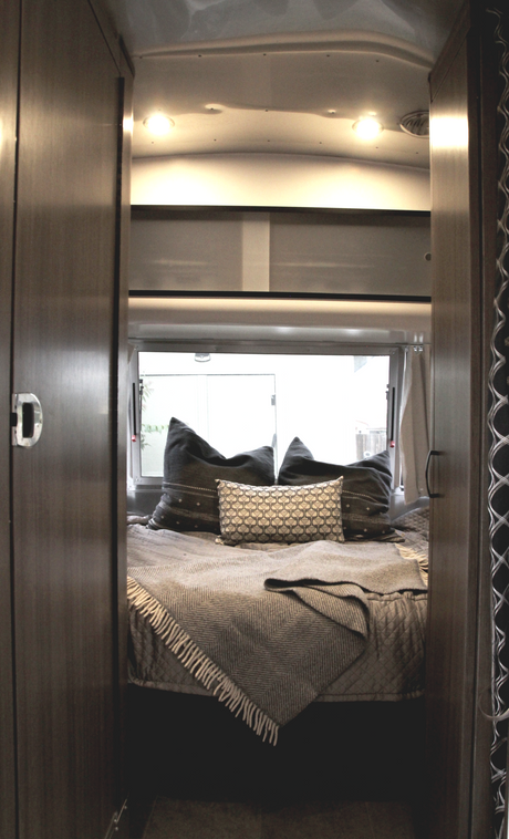 Inside an RV rental: a modern bedroom with a bed, patterned pillows, and a throw, seen from a warm wooden doorway.