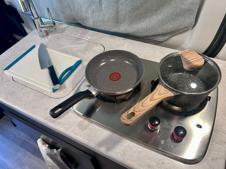 RV rental kitchen: sink, cutting board with knife, 2-burner stovetop with pan/pot. Note: 'UNIT HAS BEEN WINTERIZED' sticker.