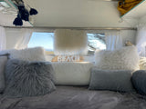 Cozy RV rental interior with fluffy pillows and a "BEACH" sign, offering a comfy escape with a view.