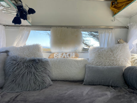 Cozy RV rental interior with fluffy pillows and a "BEACH" sign, offering a comfy escape with a view.