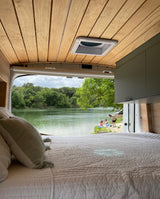 Relax by the lake! This cozy rv rental offers a stunning view from bed, with people enjoying the water's edge and lush trees.