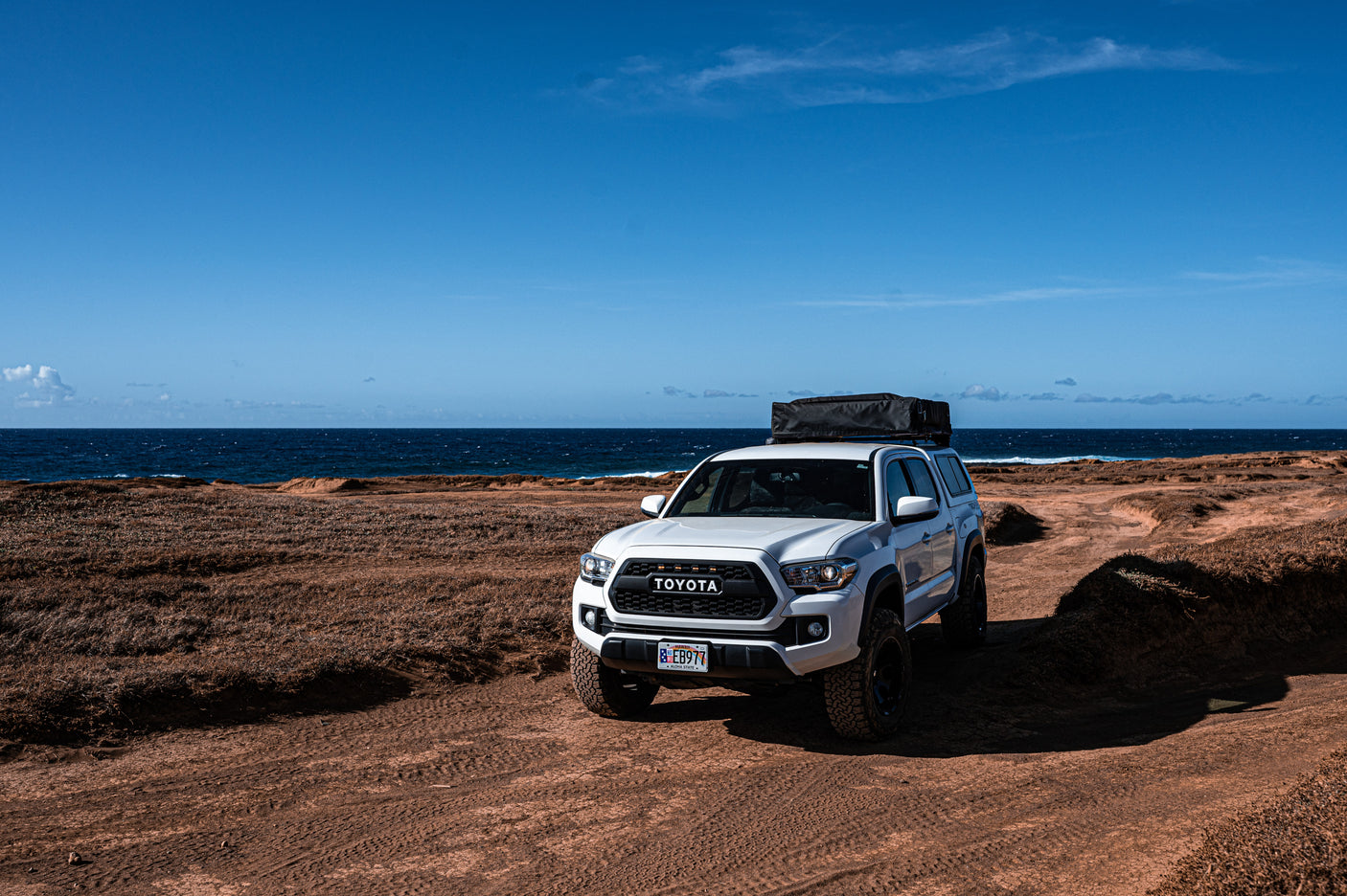 White Toyota Tacoma truck with rooftop tent on an arid coastal dirt track, ideal for your next RV rental adventure.