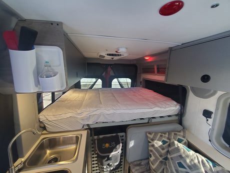 Inside an RV rental featuring a comfy bed, kitchen sink, overhead storage, and geometric pillows.